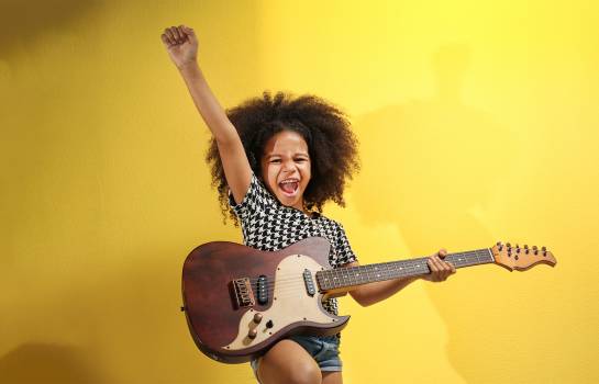 petite fille avec une guitare éléctrique sur fond jaune