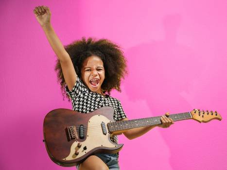 petite fille avec une guitare éléctrique sur fond mauve